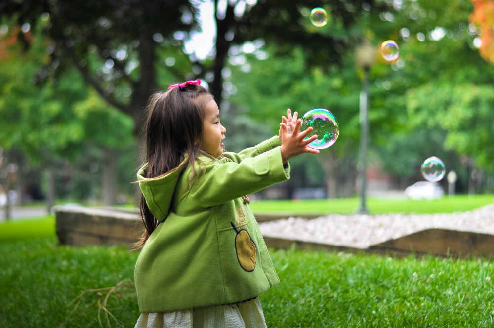 Meisje speelt met zeepbellen in park (foto door Leo Rivas)