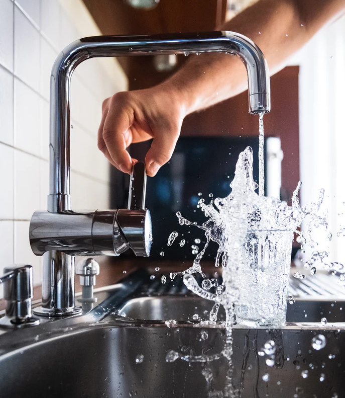 Een drinkglas dat met kraanwater gevuld wordt en heftig overloopt 