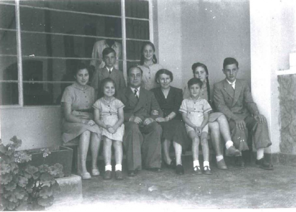 Familiefoto buiten aan het huis in Elizabeth, met de "boy" binnen achter het raam.