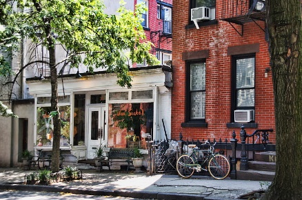 A cosy street, of which two houses are visible, a tree, a bike parked near one of both buildings.