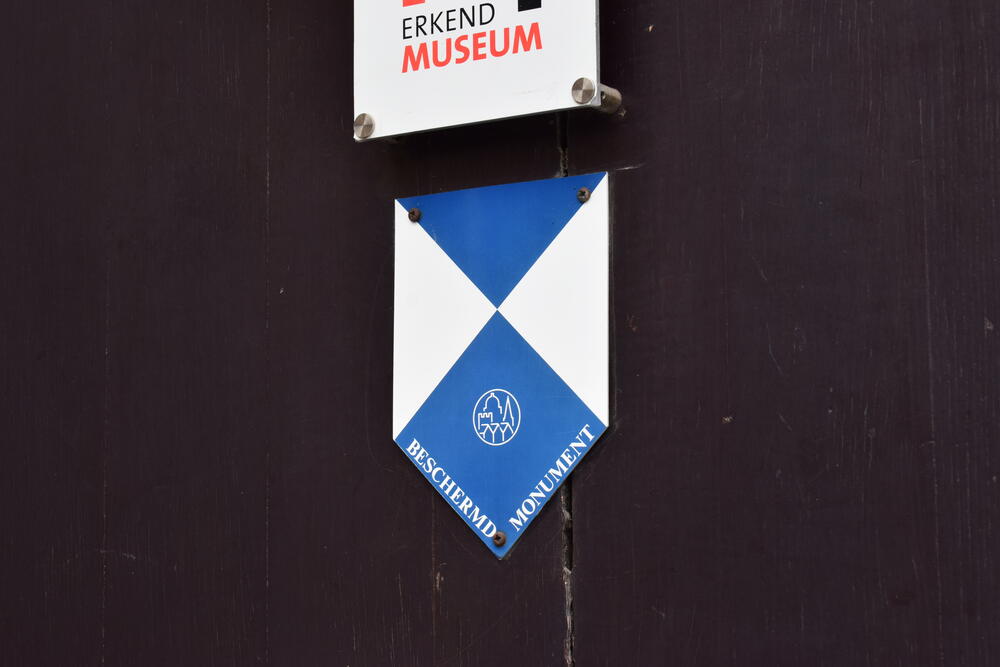 Afbeelding van het Blauwe Schild-embleem op een deur van een beschermd monument, symbool voor cultureel erfgoed dat beschermd wordt onder de Conventie van Den Haag (1954).